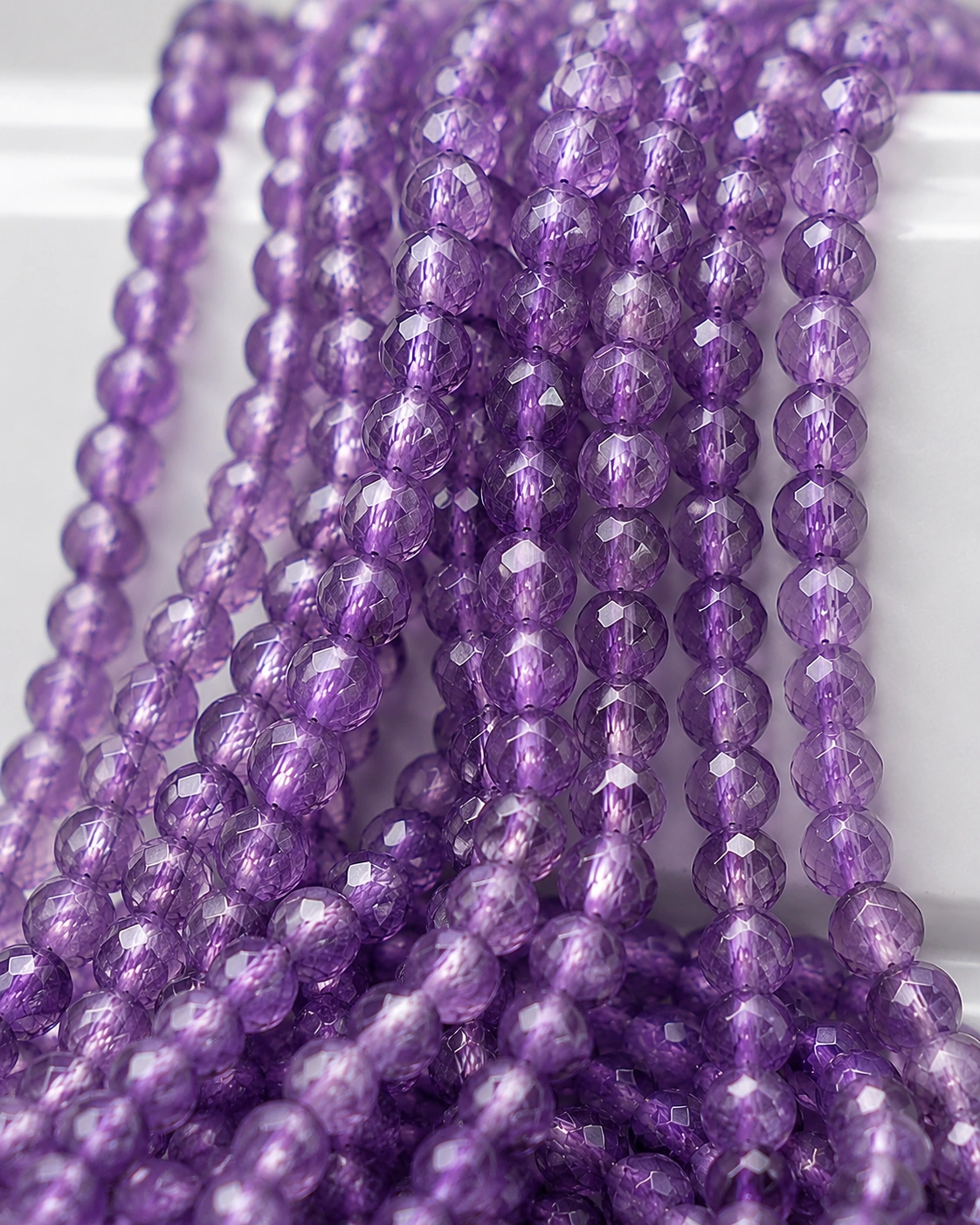 A macro-photographed image of several strands of amethyst gemstone beads atop a porcelain prop.