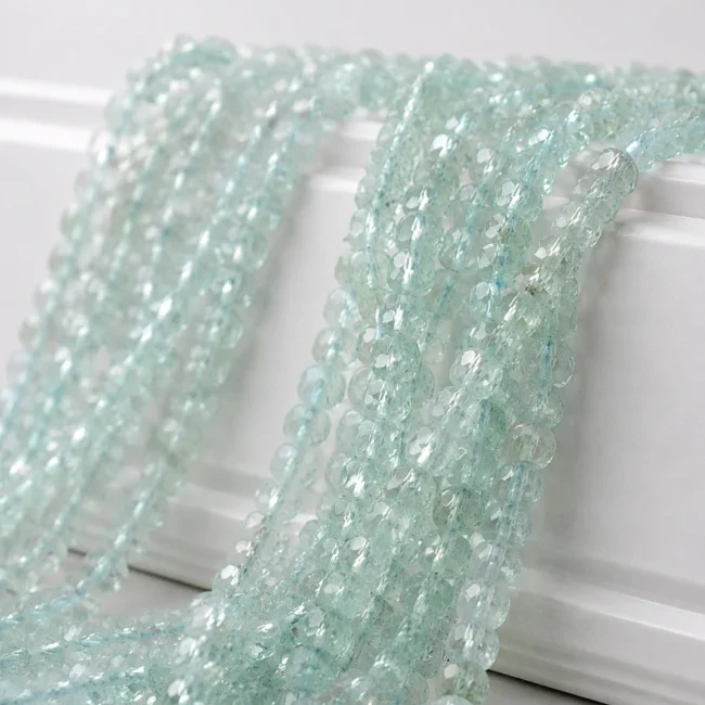 A macro-photographed image of several strands of aquamarine gemstones atop a porcelain prop.