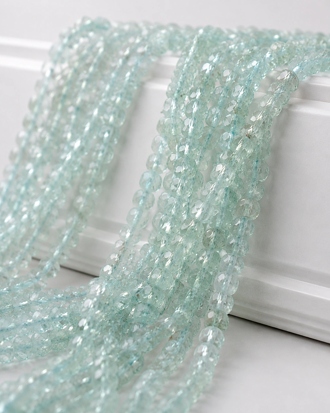 A macro-photographed image of several strands of aquamarine gemstones atop a porcelain prop.