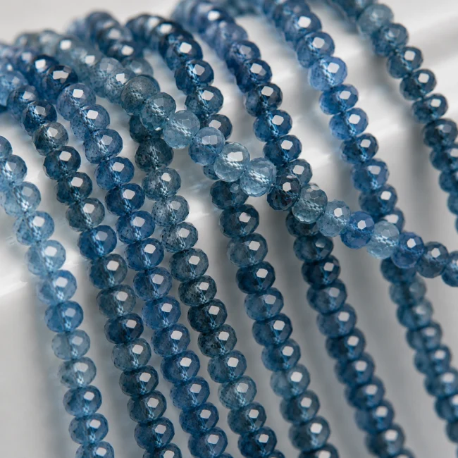 A macro-photographed image of several strands of natural London Blue topaz gemstone beads atop a porcelain prop.