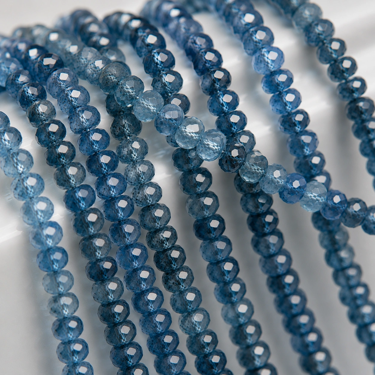 A macro-photographed image of several strands of natural London Blue topaz gemstone beads atop a porcelain prop.
