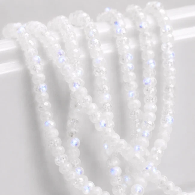 A macro-photographed image of several strands of rainbow moonstone gemstones atop a porcelain prop.
