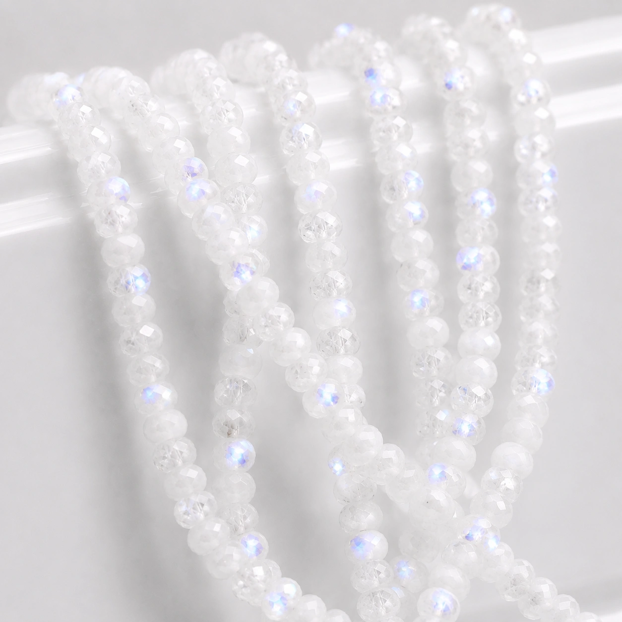 A macro-photographed image of several strands of rainbow moonstone gemstones atop a porcelain prop.