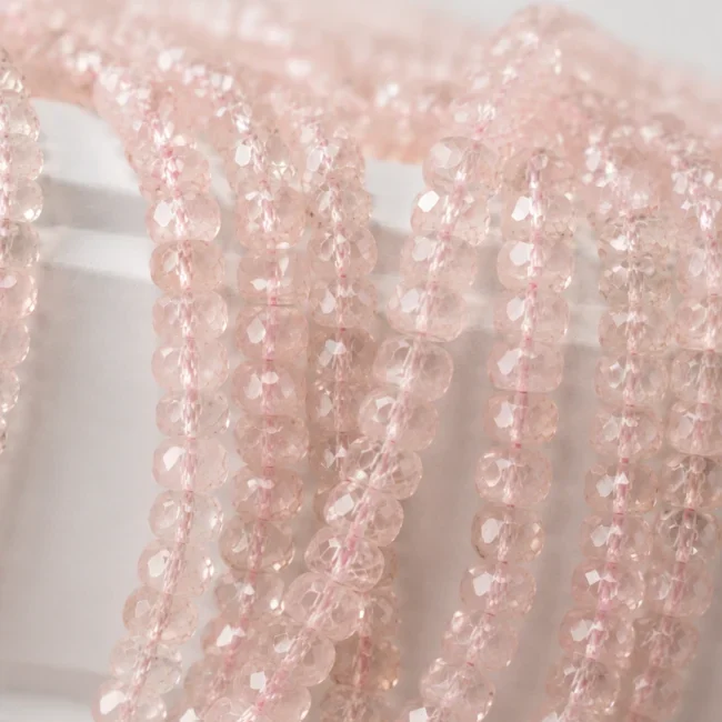 A macro-photographed image of several strands of naturally peachy-pink morganite gemstone beads atop a porcelain prop.