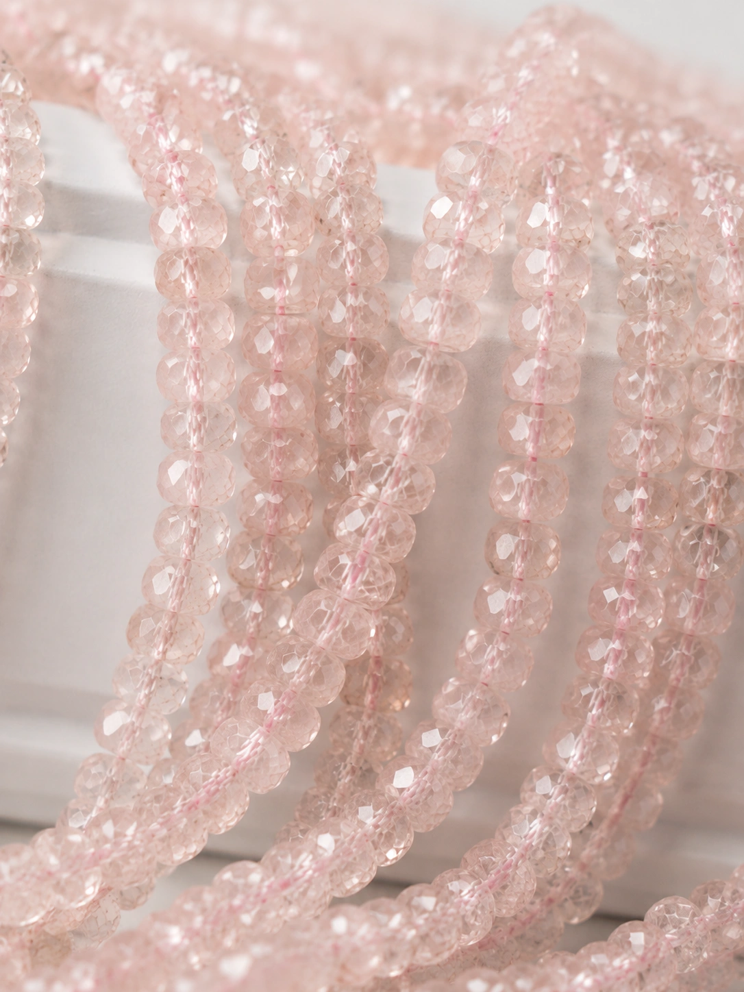 A macro-photographed image of several strands of naturally peachy-pink morganite gemstone beads atop a porcelain prop.