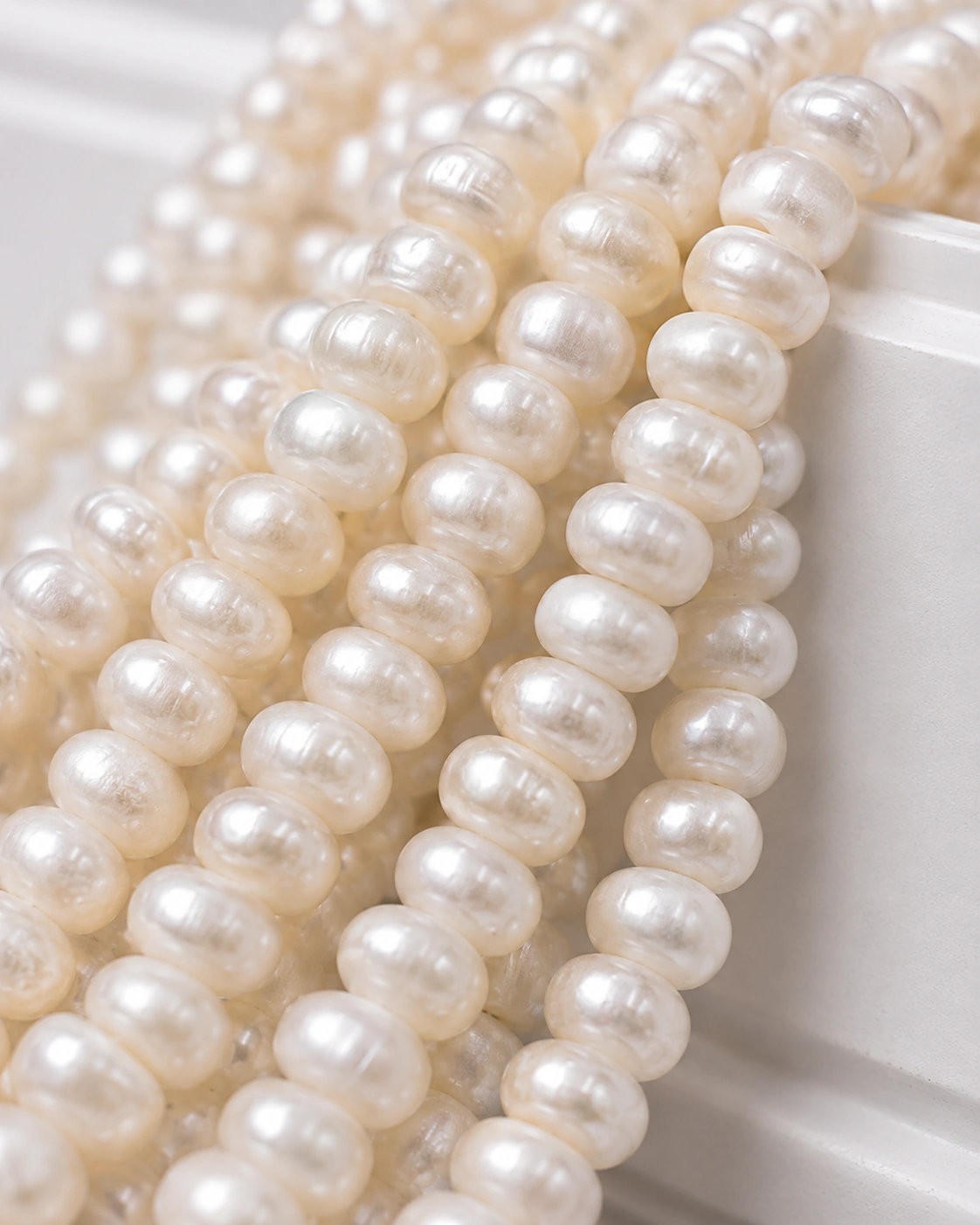 A macro-photographed image of several strands of the freshware variety of pearls atop a porcelain prop.