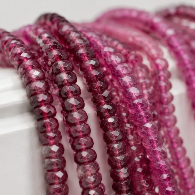 A macro-photographed image of several strands of rhodolite variety of garnet gemstones atop a porcelain prop.