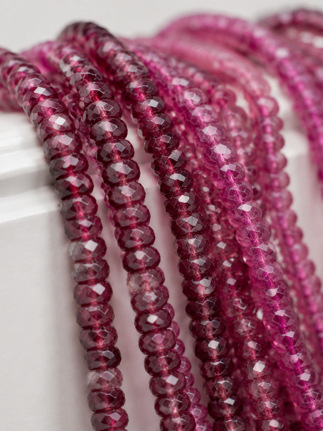 A macro-photographed image of several strands of rhodolite variety of garnet gemstones atop a porcelain prop.