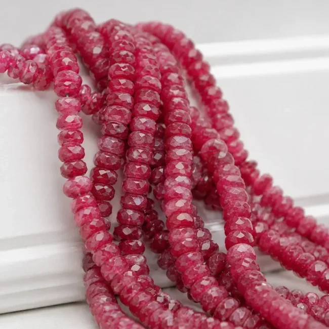A macro-photographed image of several strands of natural Longido ruby gemstone beads atop a porcelain prop.