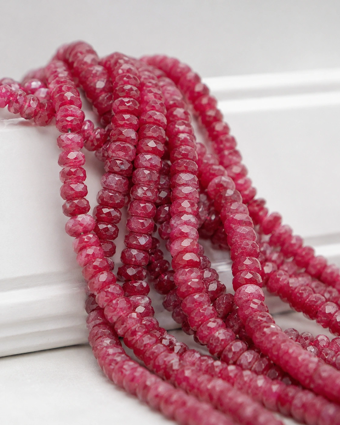 A macro-photographed image of several strands of natural Longido ruby gemstone beads atop a porcelain prop.