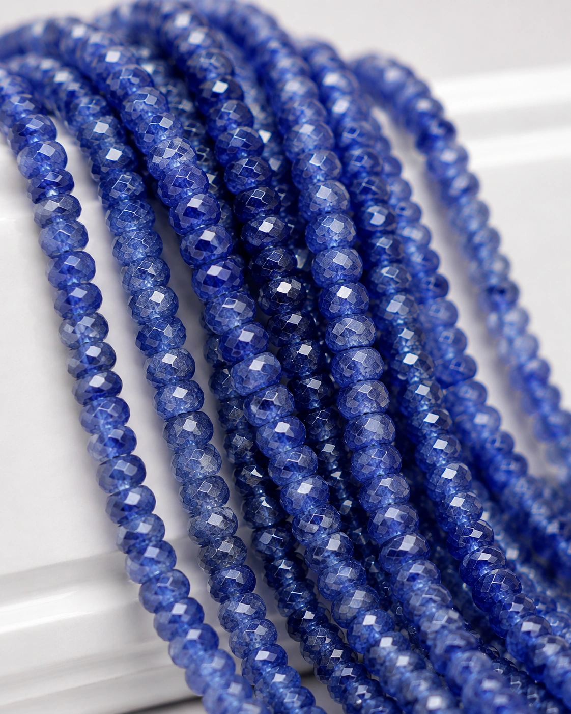 A macro-photographed image of several strands of high quality sapphire gemstone beads atop a porcelain prop.