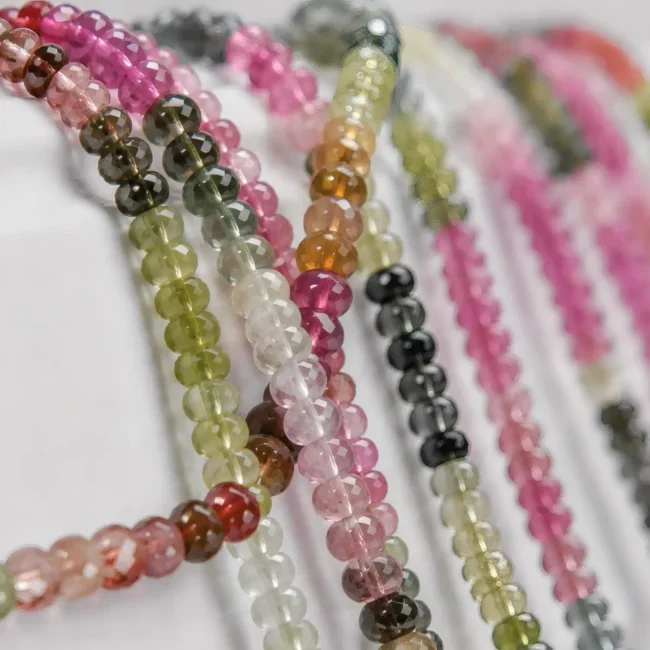 A macro-photographed image of several strands of multicolored watermelon tourmaline gemstone beads atop a porcelain prop.