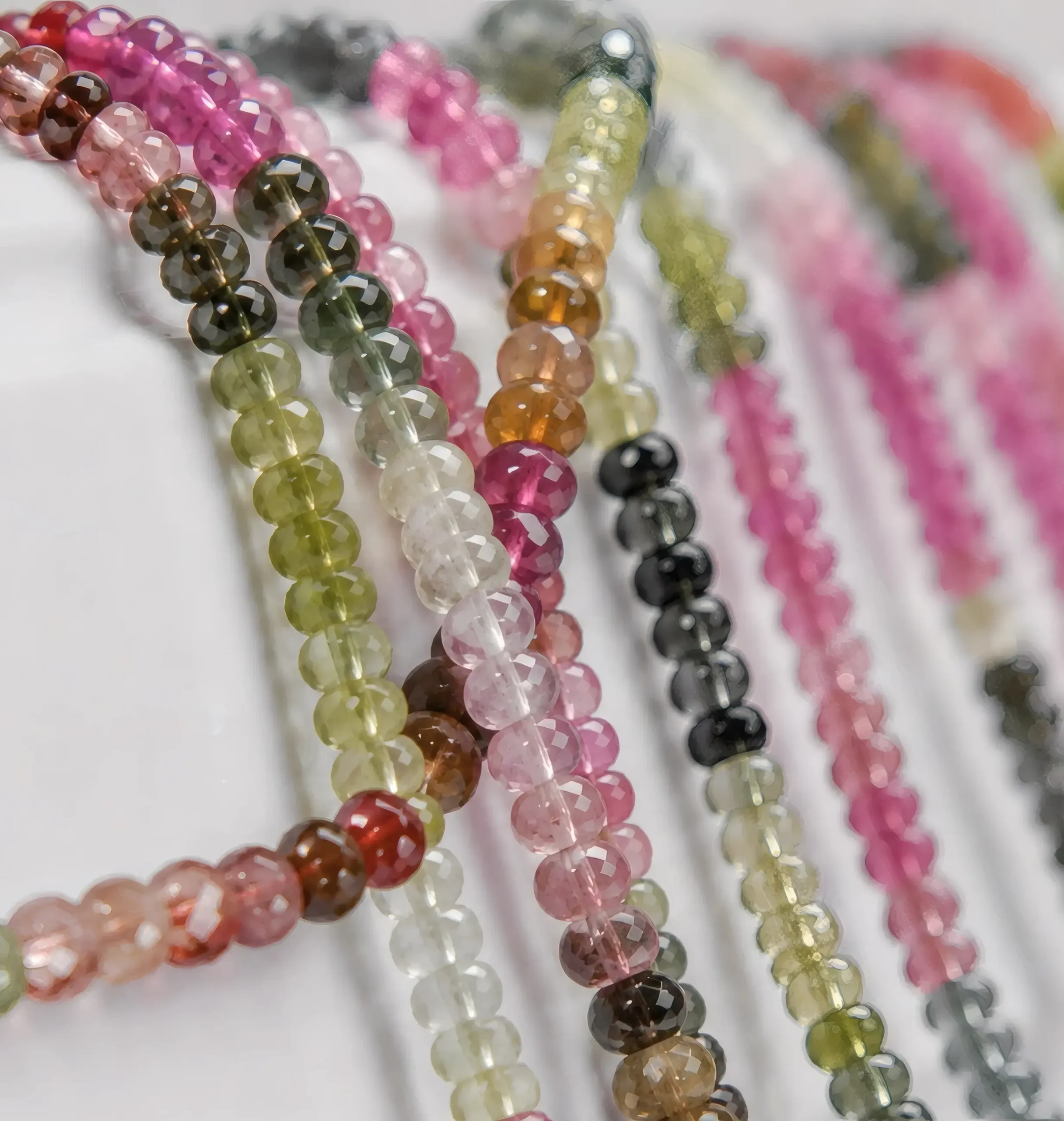 A macro-photographed image of several strands of multicolored watermelon tourmaline gemstone beads atop a porcelain prop.